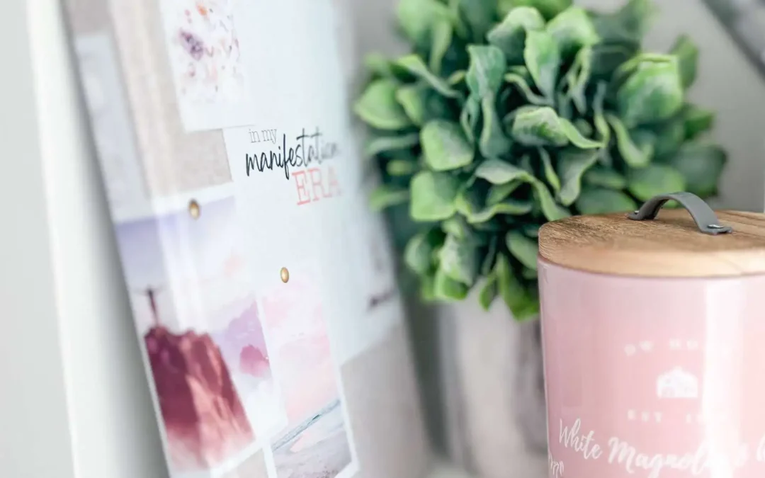 In My Manifestation Era journal on a shelf beside a pink candle and greenery.