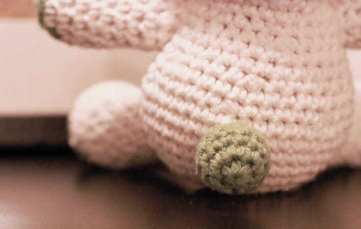 A close up picture of the back side of the crocheted bunny featuring a tiny little green crocheted ball for the bunny tail.