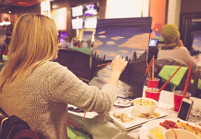 A blond hair woman painting a canvas.