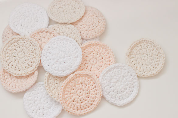 A bunch of crocheted cotton reusable makeup remover pads on a white counter top.