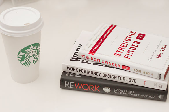 three books titled, 'StrengthsFinder2.0', 'Work for Money, Design for Love' and 'ReWork', on a table beside a white starbucks cup.