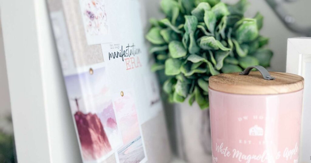 A beige and pink notebook on a shelf with some greenery and a pink candle.