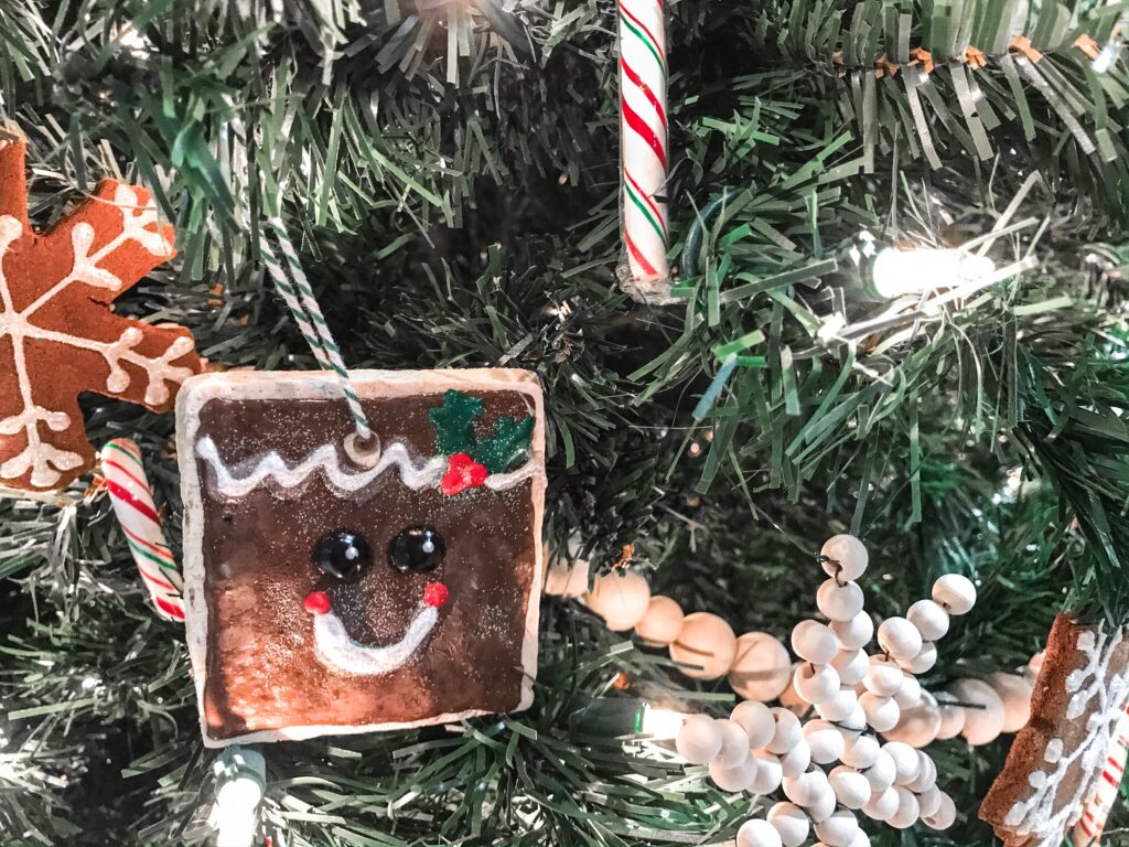 A close up of a square salt-dough christmas ornament on the tree. it's painted with puffy paint so it looks like a sugar cookie.