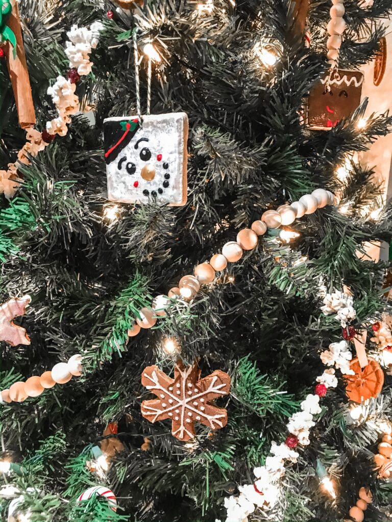 A close up of a christmas tree covered in handmade ornaments. The ornament in focus is a cinnamon dough snowflake with sparkly puffy painted details.