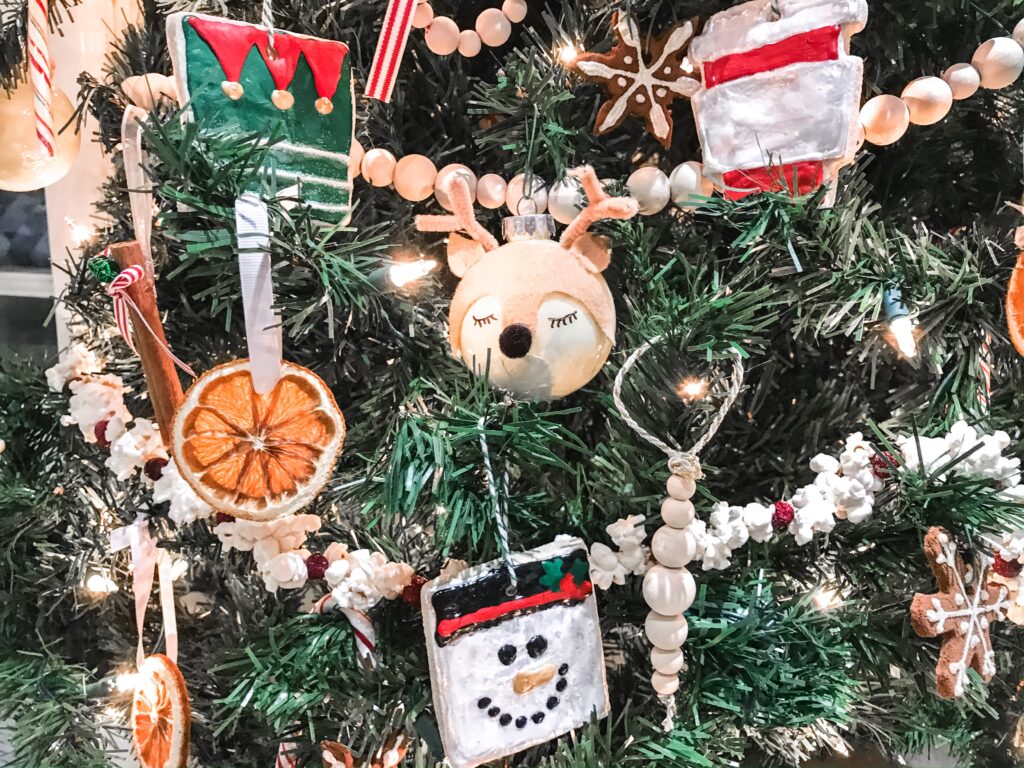 A close up of a christmas tree with many handmade ornaments, including bulbs that look like deer, dried oranges with ribbon, and ornaments painted with puffy paint.