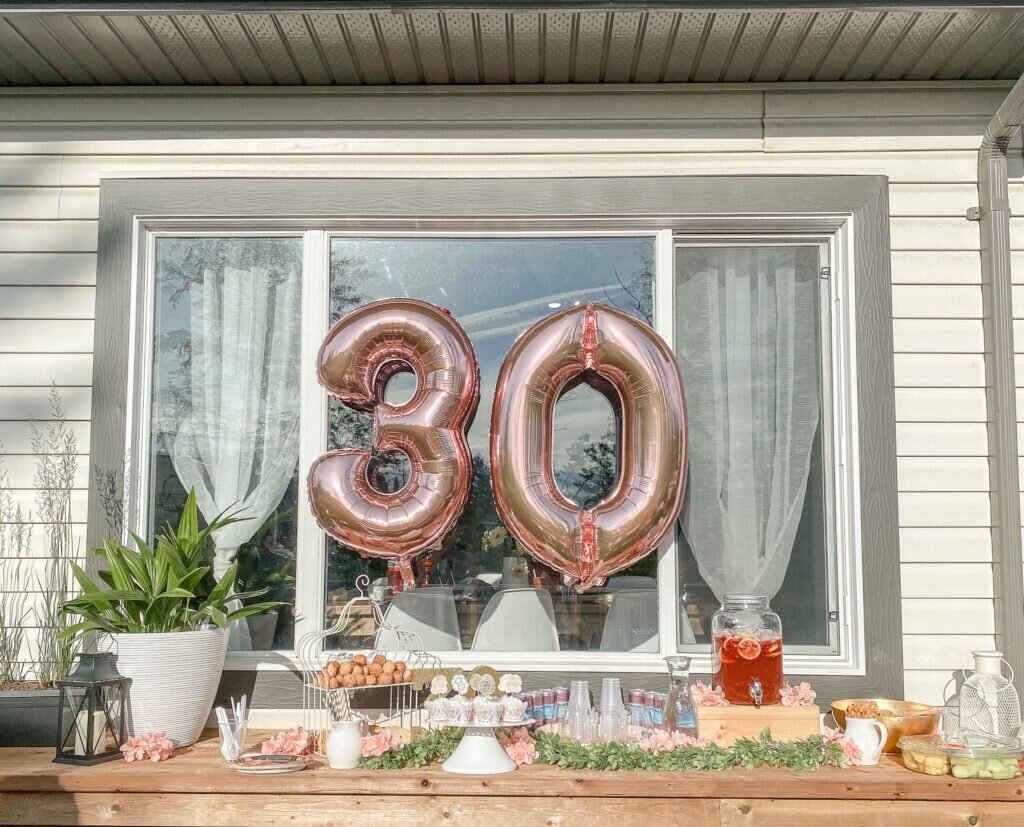 A creative 30th birthday with a beautiful pink, gold, and beige aesthetic, a giant pink metallic 3 and 0 balloon hanging in the window. 